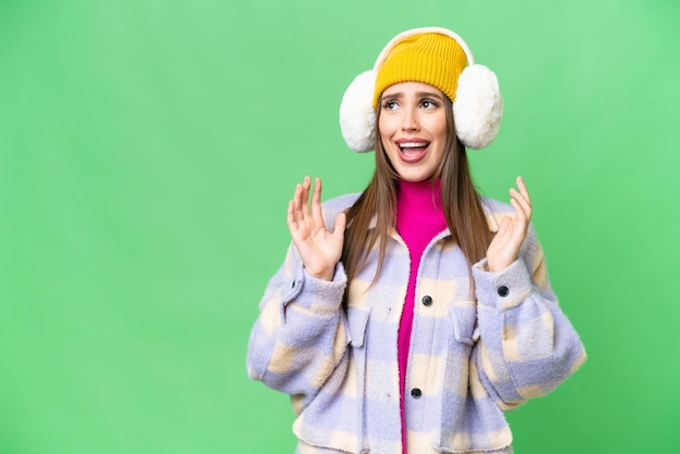 Mujer joven con manguitos de invierno sobre un fondo clave de croma aislado con expresión facial sorpresa