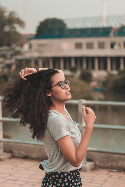 Foto mujer joven con la mano en el cabello mirando lejos de pie contra la barandilla