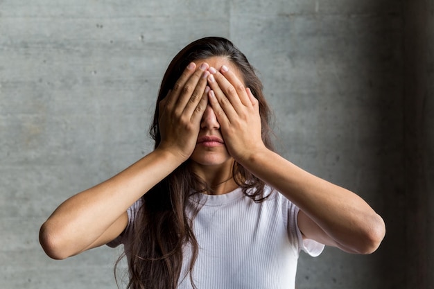 Mujer joven con las manos cubriendo los ojos contra la pared