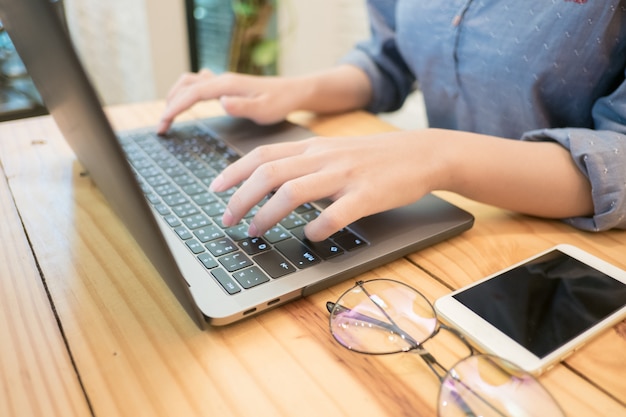 Mujer joven manos escribiendo computadora portátil en café