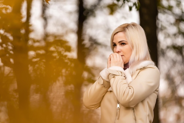 Mujer joven con las manos juntas, rezando oración, de pie en la naturaleza en otoño