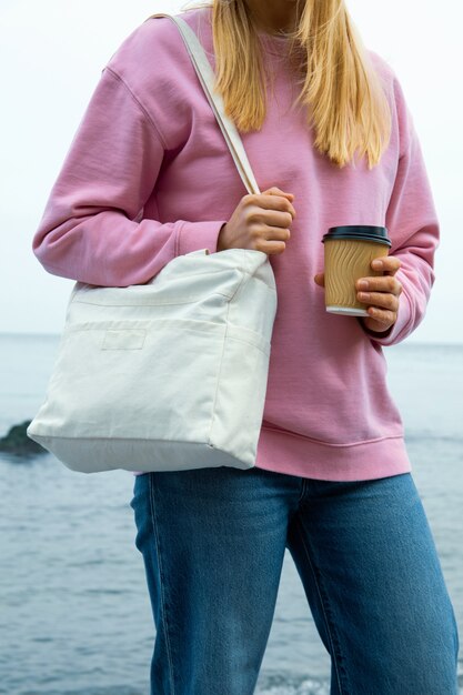 Mujer joven mantenga elegante bolsa ecológica y vaso de papel contra el mar