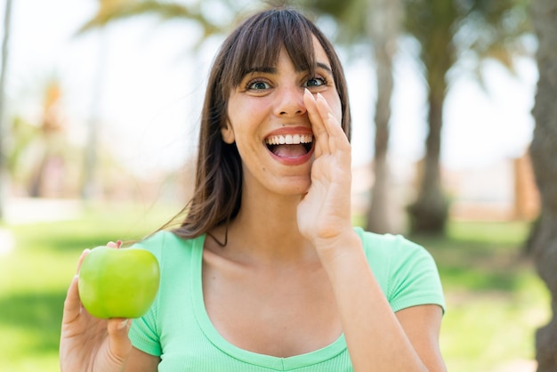 Foto mujer joven con una manzana al aire libre gritando con la boca abierta