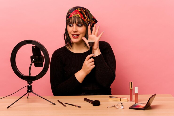 Foto mujer joven maquilladora haciendo un tutorial de maquillaje aislado sobre fondo rosa