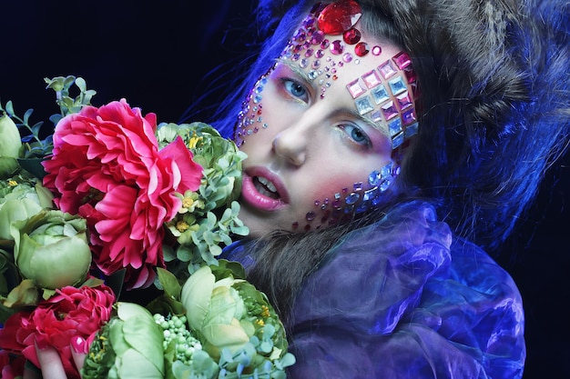 mujer joven con maquillaje creativo sosteniendo flores