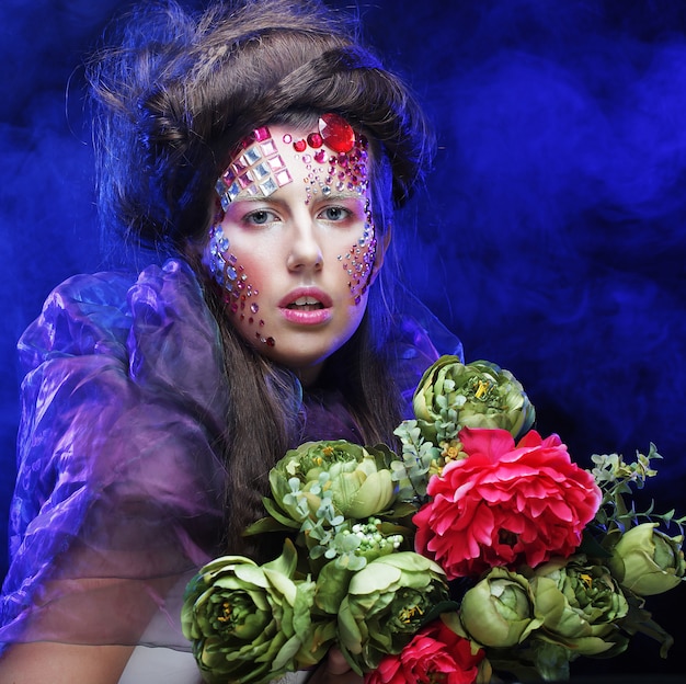 mujer joven con maquillaje creativo sosteniendo flores