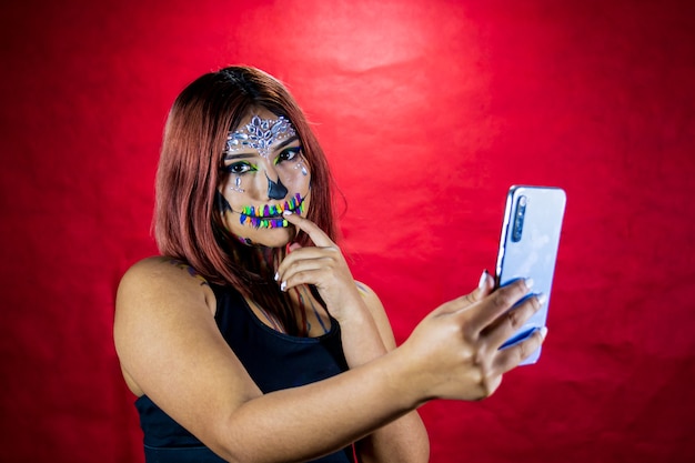 Mujer joven con maquillaje para fiesta de halloween toma un selfie desde su teléfono celular