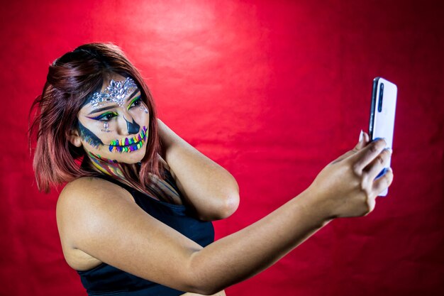 Mujer joven con maquillaje para fiesta de halloween toma un selfie desde su teléfono celular