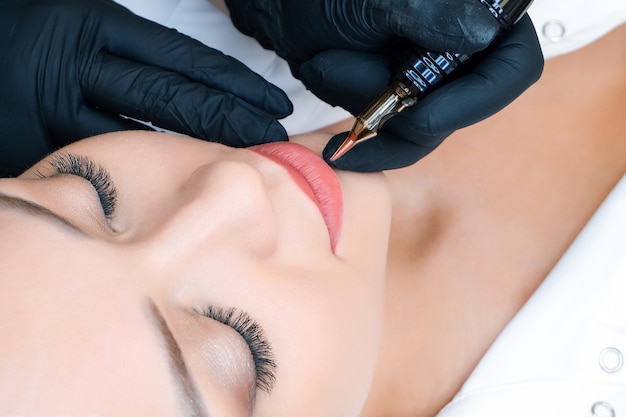 Mujer joven con maquillaje permanente en los labios en el salón de esteticistas. Fondo verde natural