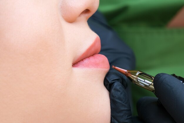 Mujer joven con maquillaje permanente en los labios en el salón de esteticistas. Fondo verde natural