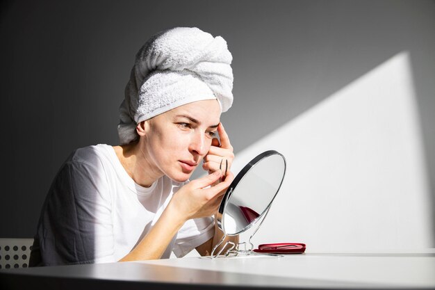 Mujer joven sin maquillaje con una toalla en la cabeza hace corrección de cejas