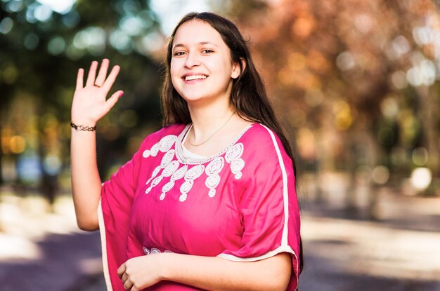 Foto mujer joven marroquí saludando y mirando a la cámara con un vestido árabe tradicional