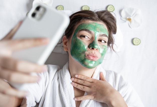 Foto mujer joven con una máscara cosmética en el rostro hace un selfie en un teléfono inteligente.