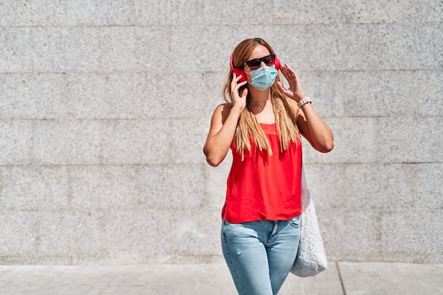 Mujer joven con una máscara escuchando música en la ciudad