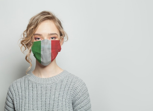 Mujer joven con una máscara facial con la bandera nacional italiana Concepto de protección contra la epidemia de gripe y el virus