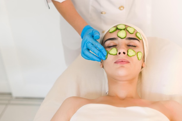 Mujer joven con máscara facial de pepino en salón de belleza. La máscara cosmética se aplica a la cara de una mujer.