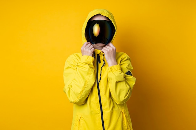 Mujer joven en una máscara de gafas cyberpunk en una chaqueta amarilla sobre un fondo amarillo