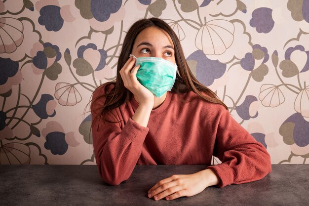 Mujer joven con máscara médica aburrida en casa. Concepto de coronavirus