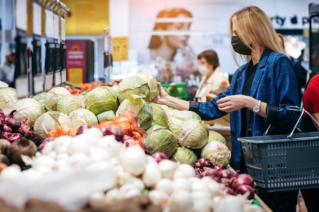 Mujer joven con máscara médica desechable de compras en el supermercado durante el brote de neumonía por coronavirus