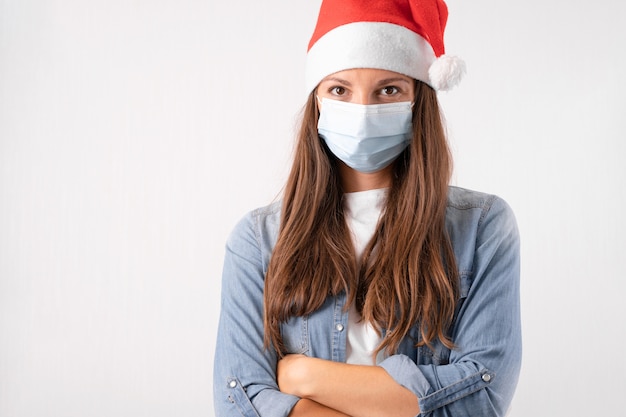 Mujer joven con máscara médica y gorro de Papá Noel sobre fondo blanco. Navidad en cuarentena. Foto de alta calidad