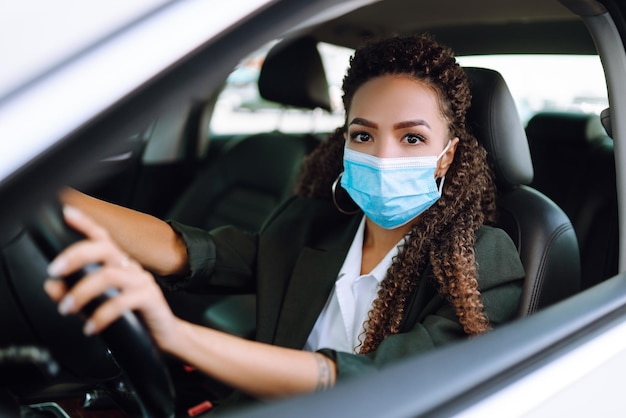 Mujer joven con máscara médica protectora conduciendo un automóvil