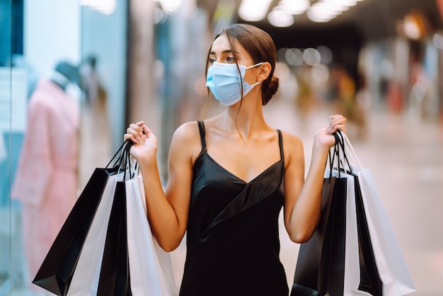 Mujer joven en máscara médica protectora estéril en su rostro con bolsas de compras en el centro comercial.