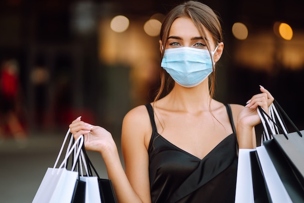 Mujer joven en máscara médica protectora estéril en su rostro con bolsas de compras disfrutando de compras.