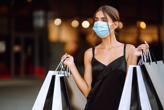 Mujer joven en máscara médica protectora estéril en su rostro con bolsas de compras disfrutando de compras.