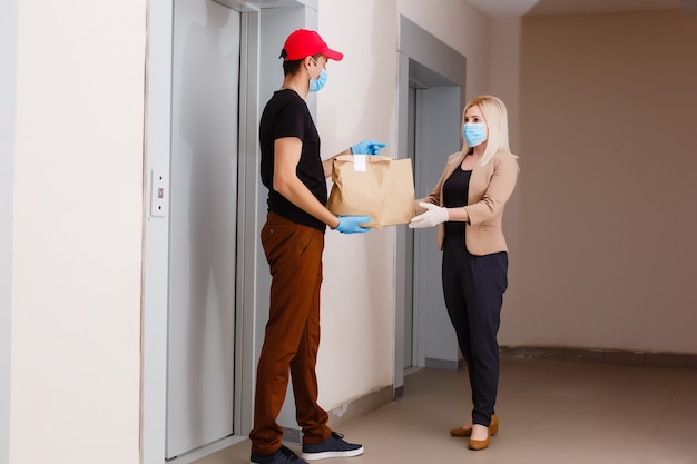 Mujer joven con máscara médica recibiendo comida ordenada del restaurante del repartidor en el interior. Prevención de la propagación del virus