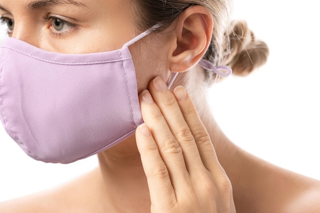 Mujer joven con máscara de prevención e irritación de la piel sobre fondo blanco. Maskne: brotes de acné por el uso de una mascarilla.