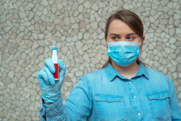 Mujer joven en una máscara protectora azul sosteniendo un spray desinfectante para manos