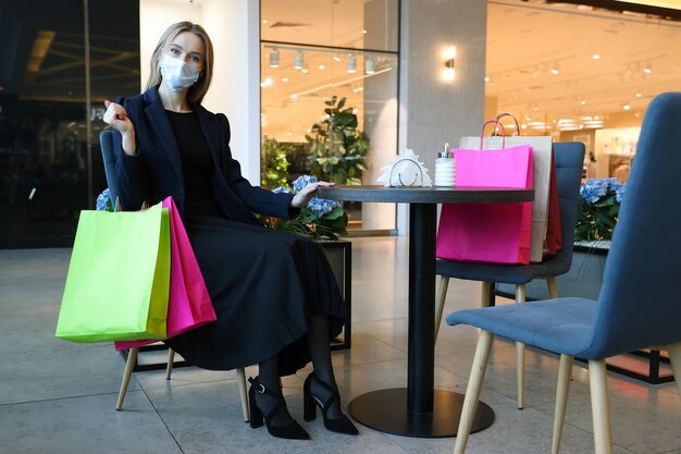 Una mujer joven con una máscara protectora después de ir de compras se sienta en un café