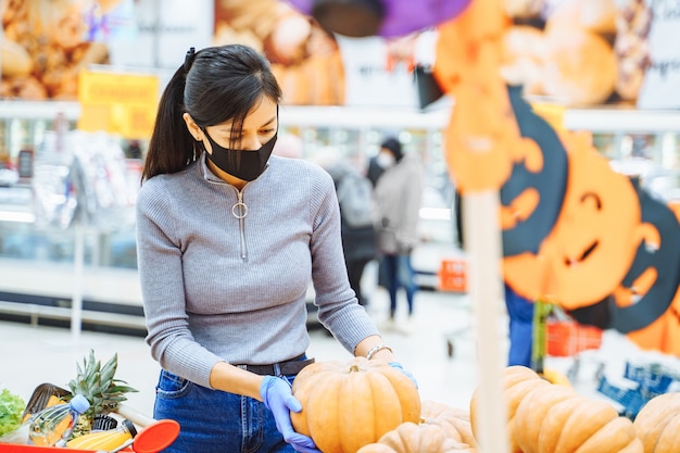 Mujer joven con una máscara protectora y guantes eligiendo calabazas para Halloween