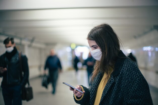 Mujer joven con una máscara protectora leyendo un mensaje de texto en una estación de metro. coronavirus en la ciudad