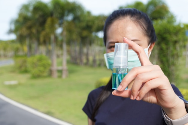 Mujer joven en máscara protectora médica y sosteniendo un alcohol en la mano. campaña para utilizar mascarilla protectora y alcohol para proteger COVID19