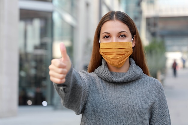 Mujer joven con máscara protectora mostrando los pulgares para arriba