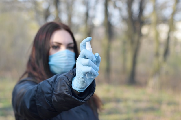 Foto mujer joven en máscara protectora muestra botella de spray desinfectante