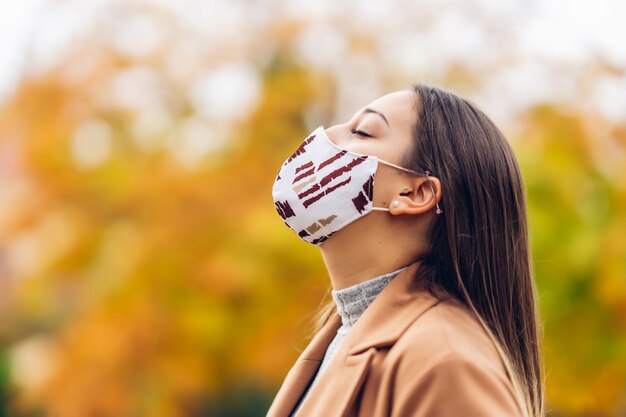 Mujer joven con una máscara protectora en el parque otoño