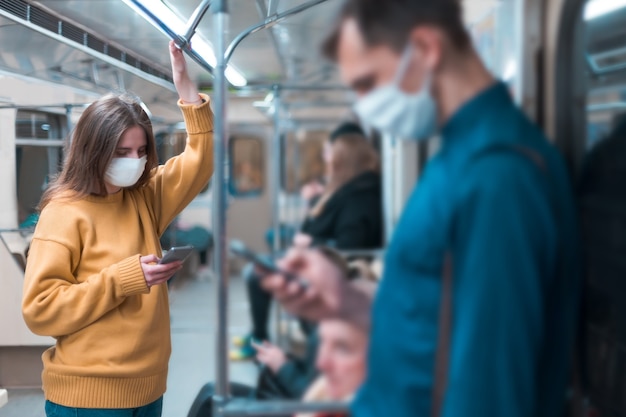 Mujer joven con una máscara protectora de pie en un vagón de metro. coronavirus en la ciudad