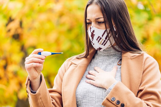 Mujer joven con una máscara protectora sosteniendo un termómetro