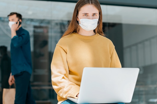 Mujer joven con una máscara protectora usa su computadora portátil en la calle. concepto de protección de la salud