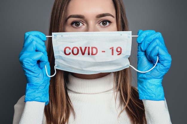 Foto mujer joven con máscara respiratoria médica con texto de coronavirus y guantes médicos azules aislados sobre gris oscuro