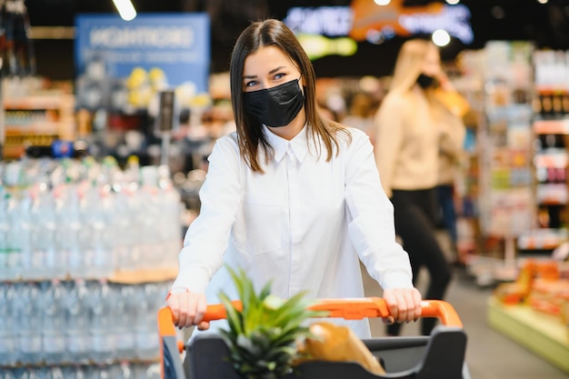 Mujer joven con mascarilla caminando por la tienda de comestibles durante la pandemia de COVID-19.