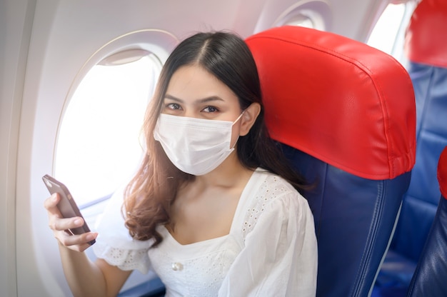 Una mujer joven con mascarilla está usando un teléfono inteligente a bordo