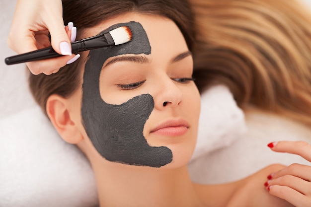 Mujer joven con mascarilla facial nutritiva en salón de belleza de cerca