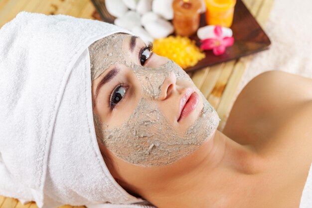 Mujer joven con mascarilla facial en el salón de spa