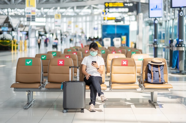 Mujer joven en mascarilla con smartphone en aeropuerto