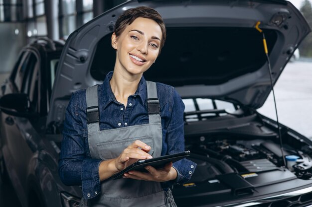 Mujer joven mecánico de automóviles revisando el auto en el servicio de autos