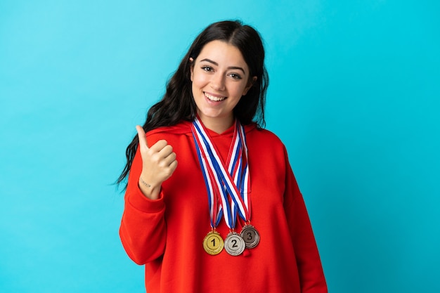 Mujer joven con medallas aislado en blanco con los pulgares hacia arriba porque ha sucedido algo bueno