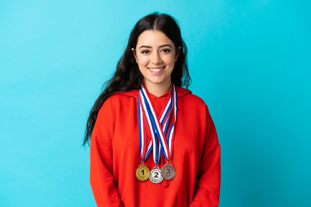 Mujer joven con medallas aislado en la pared blanca sonriendo mucho